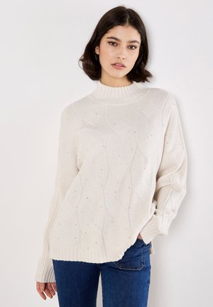 Pull en tricot de couleur crème avec un col ras du cou côtelé, un motif en diamant texturé et de petites perles décoratives sur la surface. Coupe ample.