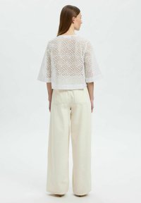 Hvid, kortærmet, perforeret top med et cropped design, parret med højtaljede, vide cremebukser. Flade sømme og minimal detaljer.