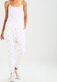 Vita joggers med små, flerfärgade triangelmönster, elastisk midja, sidofickor och smalnade vristhämmor. Matchas med beige sneakers.