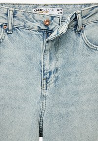 Vaqueros de denim azul claro con un corte holgado, que presentan herrajes de cobre, una cremallera estándar y una textura desgastada y desvaída. La etiqueta muestra la talla W27 L32.