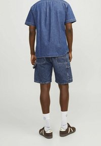 Denim-paita ja cargo-shortsit sinisenä, joissa on lyhyet hihat, rento istuvuus ja takataskut. Yhdistetty valkoisiin sukkiin ja ruskeisiin kenkiin.