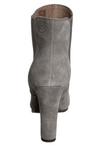 Szary zamszowy botek na wysokim obcasie, widoczny od tyłu, z widocznym przeszyciem i wytłoczonym logo „Scholl” w pobliżu górnej krawędzi.