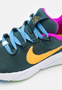 Bežecká obuv Nike s tmavozeleným zvrškom s rebrovou textúrou, jasne oranžovým logom, modrými šnúrkami a ružovým akcentom na golieri.