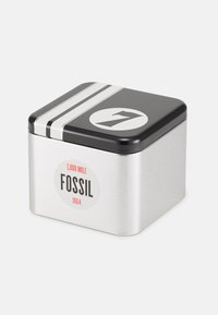 Boîte de rangement en métal avec un couvercle noir, ornée de bandes argentées et d'un logo circulaire indiquant "1,000 MILE FOSSIL 1954" en rouge et noir.