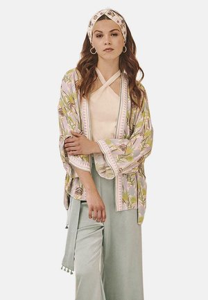 Chaqueta estilo kimono en rosa claro, con patrones florales, combinada con una blusa crema y pantalones de pierna ancha en verde menta, de textura suave.