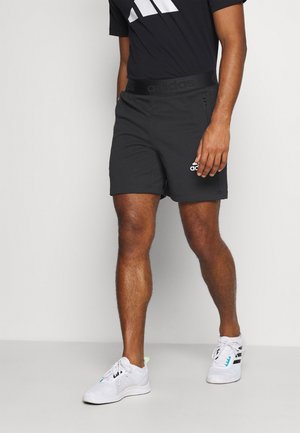 Pantaloni sportivi neri con cintura elastica che presentano il marchio 'adidas', abbinati a sneakers bianche in rete e una t-shirt nera con un logo.