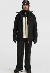 Vyriška juoda slidinėjimo striukė su oranžiniais akcentais, priekyje užtrauktukas ir kišenių detalės, derinama su juodomis kelnėmis ir pirštinėmis. Komplekte yra šalmas ir akiniai.