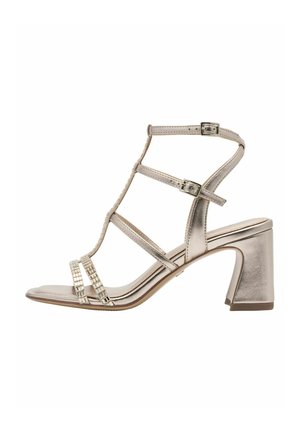 Sandalo argentato metallizzato con tacco a blocco alto, caratterizzato da un design con cinturini, fibbie alla caviglia e cinturini decorativi con perline. Suola piatta.