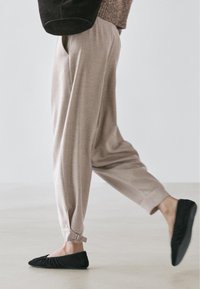 Beige smalle bukser med elastisk manchet, tekstureret stof, kombineret med sorte flade sko med en rynket detalje.