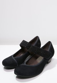 Chaussures en suède noir avec des orteils arrondis, de petits talons et une sangle décorative ornée de strass sur le dessus. Fini texturé.