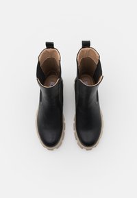 Botas de tobillo de cuero negro con una textura suave, paneles laterales elásticos y suelas de goma beige gruesas. Diseñadas para un fácil calzado.