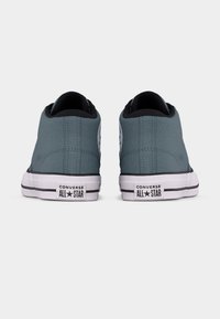 Par natikača Converse All Star sive boje prikazanih sa stražnje strane, s crnim obrubom i bijelim gumiranim potplatima s logotipom.