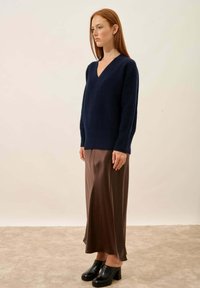 Granatowy sweter dzianinowy z dekoltem w serek, w zestawieniu z brązową satynową spódnicą midi i czarnymi klamrami na grubym obcasie, stojący na neutralnym tle.