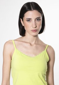 Canottiera verde lime con spalline sottili e bordo in pizzo scallop lungo il décolleté, realizzata in un tessuto morbido e leggero.