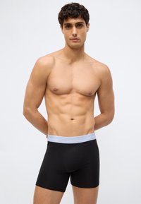 Svarta boxerkalsonger av ett slätt material med en ljusgrå Calvin Klein-logga på midjebandet, med en åtsittande design och utan synliga mönster.