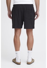 Black shorts made of textured fabric with an elastic waistband, featuring a single back pocket and a relaxed fit.
