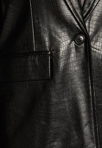 Blazer de cuero sintético negro, texturizado con un patrón de cocodrilo, con cierre de un solo botón y un bolsillo en el pecho.