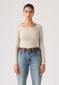 Μπεζ μακρυμάνικο τοπ με ριμπ υφή και τετράγωνο ντεκολτέ, σε συνδυασμό με ανοιχτό μπλε ψηλόμεσα τζιν και καφέ ζώνη με χρυσή αγκράφα.