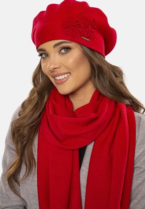 Red knit beret with floral accents, paired with a matching red scarf. Soft texture, rounded shape, and smooth finish create a cohesive look.