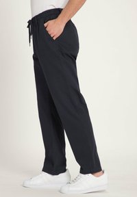 Marineblaue elastische Hosen mit Bindegürtel, Seitentaschen, verjüngten Beinen und glatter Textur, kombiniert mit weißen Sneakers.