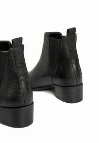 Botas de tobillo de cuero negro con acabado texturizado, paneles laterales elásticos y tacones bloques redondos. Cuenta con tiradores para facilitar su uso.