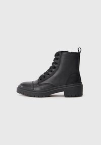 Botas de tobillo de imitación cuero negro con punta redondeada, parte delantera con cordones, lengüeta y suela de goma gruesa con un patrón de textura.