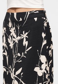 Gros plan sur une taille portant une jupe noire à imprimé floral beige et un top court blanc, dévoilant le ventre et les détails de la jupe.