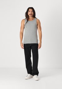 Top din bumbac gri, fără mâneci, cu guler rotund, asociat cu blugi negri din denim. Modelul stă pe un fundal simplu, purtând adidași albi.