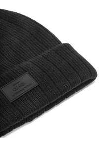 Czarna dziana czapka z prążkowanym wzorem. Posiada wyraźną prostokątną czarną skórzaną metkę z wytłoczonym tekstem.
