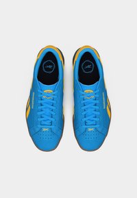 Par modrih in rumenih Reebok superg z vezalkami, videnih od zgoraj na enostavni belem ozadju.