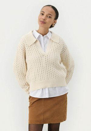 Cream knit sweater with a large collar and v-neck, featuring an open weave pattern; paired with a white shirt and brown skirt.