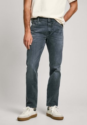 Tummanharmaat farkut suoran leikkauksen, denim-materiaalin, hienovaraisen kulutuksen ja viiden taskun kera, yhdistettynä valkoisiin lenkkareihin ja vaaleaan paitaan.