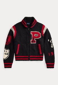 Μαύρο πλεκτό varsity πουλόβερ με φερμουάρ με κόκκινες και άσπρες ρίγες, ένα μεγάλο κόκκινο και άσπρο γράμμα Π και διάφορα κεντημένα patches στα μανίκια.
