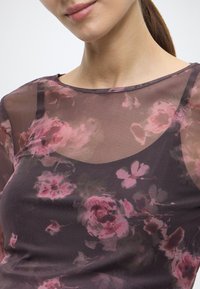 Διαφανές τοπ από μεσοφόρι με λουλουδένιο μοτίβο σε αποχρώσεις του ροζ και σκούρου μωβ. Στρογγυλή λαιμόκοψη και διάφανη, ελαφριά υφή.
