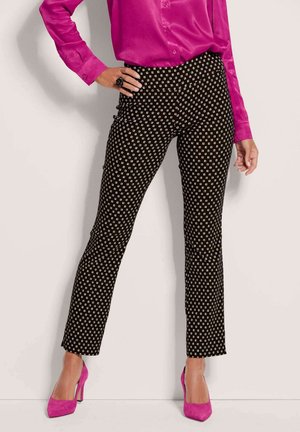Schwarz gemusterte Hose mit weißen quadratischen Akzenten, kombiniert mit einer leuchtend pinken Satinbluse und passenden hohen Schuhen.