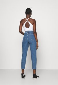 Body blanco con abertura en la espalda, combinado con unos vaqueros de mezclilla azul de talle alto. Los vaqueros tienen una pierna estrecha y cuentan con bolsillos traseros.