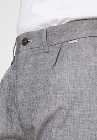 Gray plaid trousers with a textured fabric, featuring a button closure, side pockets, and subtle pleats at the waist.
