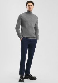 Grijs coltrui met een gestructureerde afwerking, gecombineerd met marineblauwe broek en zwarte stevige veterschoenen, wat zorgt voor een contrast in kleuren en stijlen.