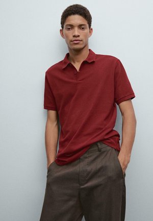 Bordeaux polo-shirt med klassisk krave og korte ærmer, lavet af glat stof. Båret med grå skræddersyede bukser. Enkel design, ingen mønstre.