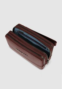 Cartera de cuero marrón con dos compartimentos con cremallera, que presenta una textura suave y acentos de cremallera de metal. El interior tiene un forro azul.