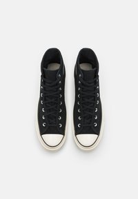 Svarta hög-top sneakers med ovandel i kanvas, vit gummitå, och metallögla; har svarta snören och vadderad krage.