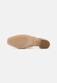 Beige suede pump shoe with a smooth, rounded toe, a narrow heel, and a textured rubber outsole featuring horizontal grooves and branding.