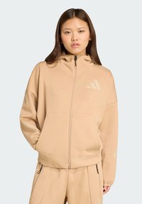 Beige rits hoodie gemaakt van zachte stof, met een hoge kraag, voorzakken en een subtiele logootje op de borst.