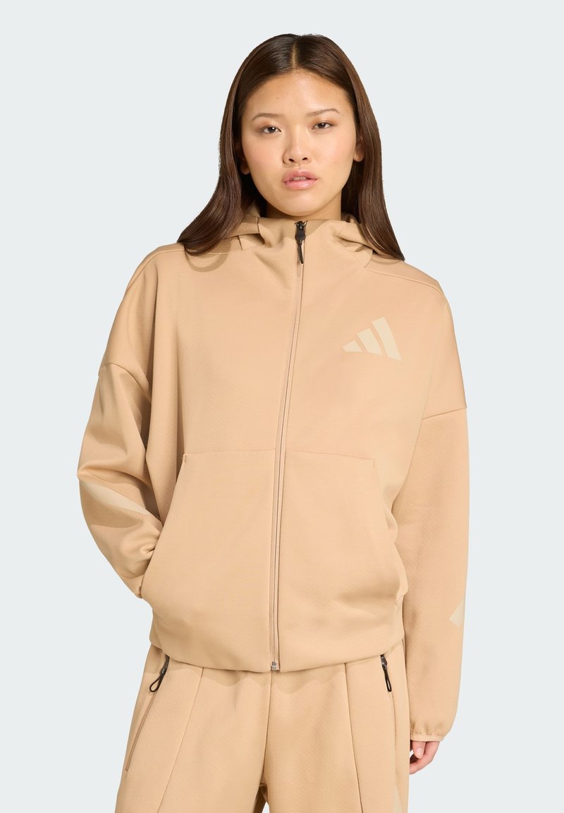 Beige rits hoodie gemaakt van zachte stof, met een hoge kraag, voorzakken en een subtiele logootje op de borst.