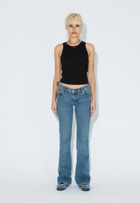 Svart ärmlös topp och blå utsvängt jeans. Toppen är åtsittande; jeansen har en klassisk fem-fickors design och en urtvungen tvätt.