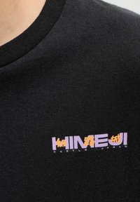 Close-up van een zwart shirt met paarse en oranje tekst waarop "KINEJI CASTLE JAPAN" staat in het Engels en Japanse karakters.