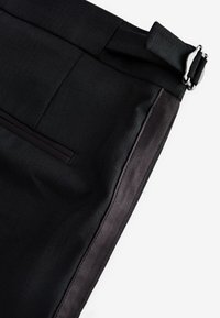 Pantaloni neri in tessuto morbido, con una tasca laterale, passanti per la cintura e una fibbia argentata sul cinturino.