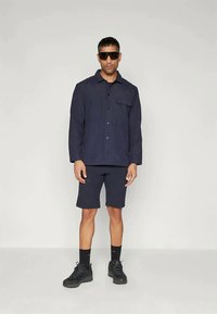 Mornarska košulja na dugmad s džepom na prsima, u kombinaciji s odgovarajućim šortsevima, crnim čarapama i čvrstim crnim tenisicama; minimalistički dizajn i prilagođeni kroj.