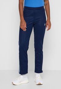 Tmavomodré teplákové nohavice z text�úrovanej tkaniny, s bočnými vreckami, priliehavým pásom a bielymi pruhmi po stranách.