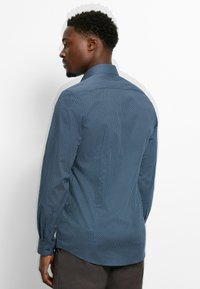 Langärmliges, blaues Hemd mit Knopfleiste und einem strukturierten, geometrischen Muster sowie einem klassischen Kragen. Verfügt über geknöpfte Ärmel und einen geschwungenen Saum.